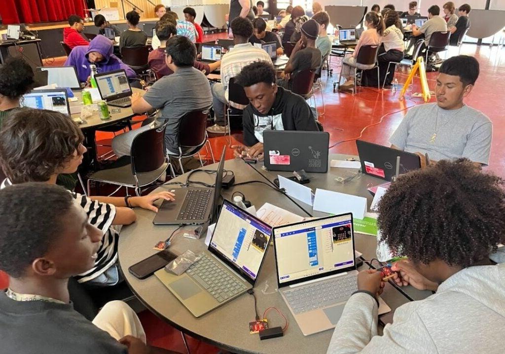 Five students sitting around round table working with Micro:Bits